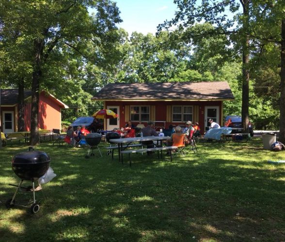 Group of people sitting at picnic tables outside red cabins surrounded by trees at Foxfire Resort On Table Rock Lake