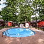Outdoor swimming pool surrounded by red cabins and tall trees at Foxfire Resort Cabins on Table Rock Lake